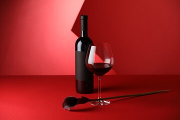 Tasty wine in bottle, glass and flower on red background