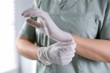 Medical worker putting on gloves in hospital, closeup