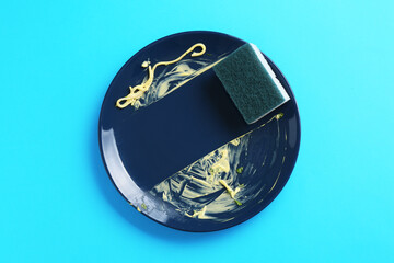 Dirty plate and sponge on light blue background, top view