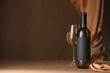 Bottle of wine, wineglass and cloth on brown table, space for text