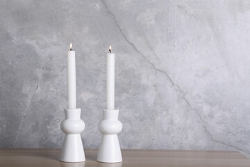 Stylish candlesticks with burning candles on wooden table near grey marble wall indoors, space for...