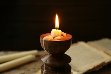 Burning candle in candlestick and old book on table, closeup