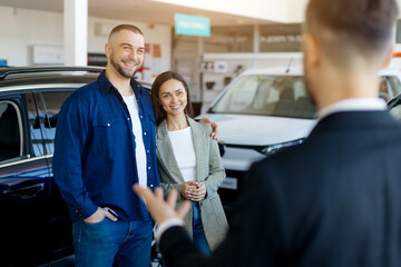 Car salesman enthusiastically presenting vehicles to a couple inside a spacious car dealership...