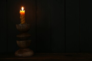 Burning candle in candlestick on wooden table