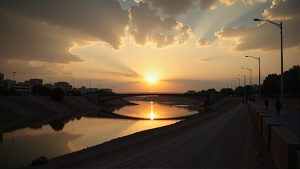 Fototapeta premium Tigris Sunsets in Iraq Baghdad over river, bridge in background, street lights illuminating road, people walking, warm orange glow, clouds. Concept of Tigris Sunsets in Iraq Baghdad landscape.