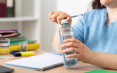 Happy female student opening a water bottle sitting in the living room at home