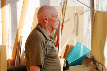 Elderly craftsman reflecting on years of artistry in a sunlit workshop filled with colorful...
