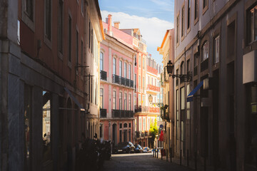 A narrow cobblestone street in Bairro Alto, Lisbon, lined with charming pastel-coloured buildings, capturing historic and picturesque atmosphere of this Portuguese neighbourhood on a sunny summer day.