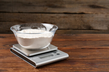 Electronic kitchen scale with bowl of flour on wooden table, closeup. Space for text