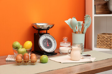 Kitchen scale, products and cooking utensils on wooden table
