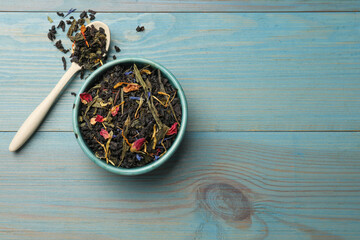 Dry tea leaves in bowl and spoon on light blue wooden table, flat lay. Space for text