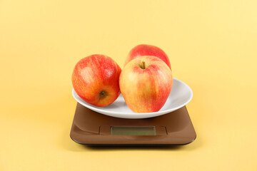 Electronic kitchen scale with apples on yellow background