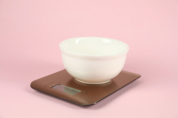 Electronic kitchen scale with bowl on pink background, closeup