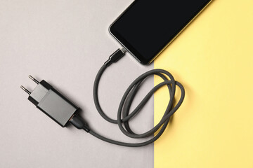 USB power adapter with charge cable and smartphone on color background, top view