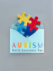 Autism World Awareness Day concept with colorful puzzle pieces in an envelope on a gray background