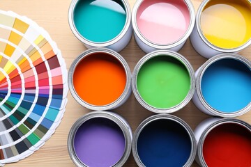 Cans of bright paints and color palettes on wooden table, flat lay