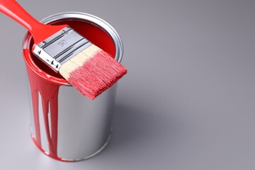 Can of red paint and brush on grey background, closeup. Space for text