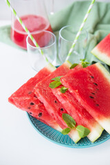 Refreshing watermelon slices with mint garnish, served on a teal plate, alongside glasses of watermelon juice and straws