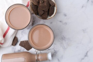Tasty chocolate milk in glasses, bottle and pieces of chocolate on white marble table, flat lay. Space for text