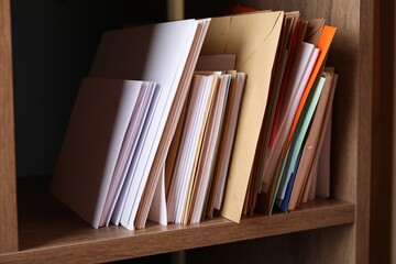 Different paper envelopes on wooden shelf in post office, closeup