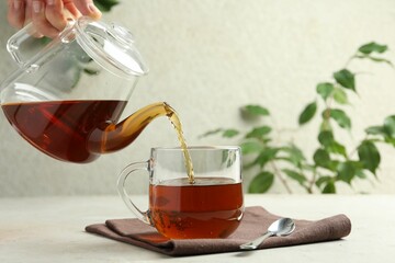 Woman pouring aromatic tea from teapot into cup at light textured table, closeup