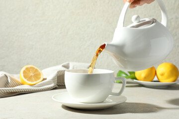 Pouring aromatic tea from teapot into cup at light textured table, closeup