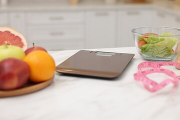 Kitchen scales, measuring tape, salad and fruits on white table indoors, closeup