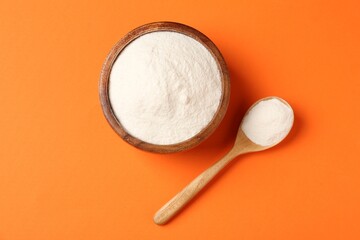 Collagen powder in bowl and spoon on orange background, flat lay