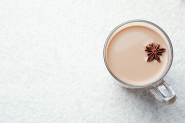 Aromatic Masala tea with anise star in glass cup on white textured table, top view. Space for text