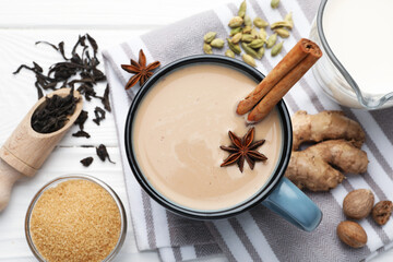 Aromatic Masala tea in cup, spices, milk and brown sugar on white wooden table, flat lay