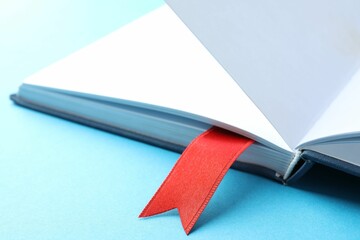 Book with red ribbon bookmark on light blue background, closeup