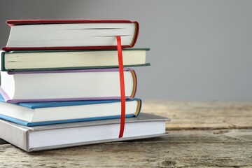Book with red ribbon bookmark and colorful ones on wooden table against grey background, closeup....