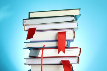 Books with red ribbon bookmarks on light blue background, closeup