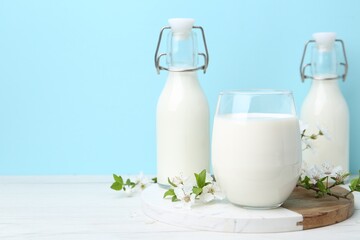 Fresh milk and blossoms on white table against light blue background. Space for text