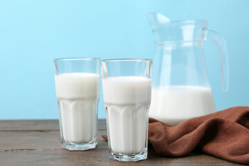 Fresh milk on wooden table against light blue background