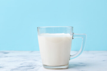 Cup of milk on white marble table against light blue background