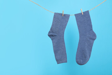 Pair of socks hanging on washing line against light blue background, space for text