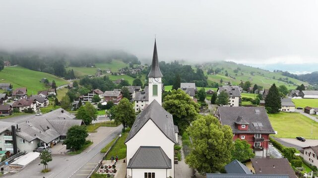 7 juli 2025, Wildhaus-Alt Sint Johann, Switzerland. Aerial view, drone flight in Wildhaus-Alt Sint Johann during cloudy summer day. Near Alpstein mountains, flight towards church in the centre of the 