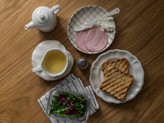 Breakfast and snack ingredients - ham, cheese, green salad, toast, green tea on a wooden table, top view