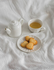A cup of green tea, shortbread cookies in the shape of a heart, a teapot on a light background