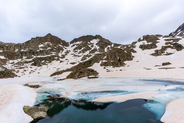 Melting snow reveals rugged peaks and frozen lakes in the Pyrenees of Lleida, Spain. A stunning contrast between winter and spring, capturing untouched nature and alpine beauty along the GR11 trail.