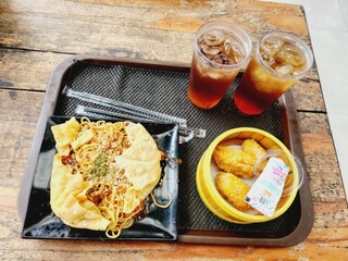 Fried noodles with dumplings and iced tea on a tray.