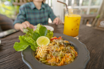 Seafood pasta plate served with green salad and lime wedge alongside tropical passion fruit juice on casual restaurant table. Person enjoying Mediterranean meal. Cuisine and relaxation meet in summer.