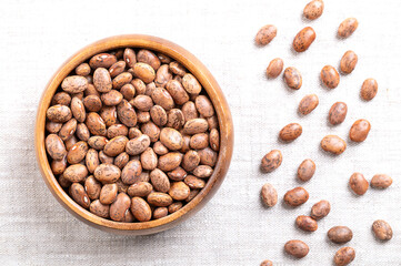 Pinto beans in a wooden bowl on linen fabric. Dried variety of common beans, Phaseolus vulgaris. Type of bean that are tan with reddish-brown specks. Most popular bean in Mexico and Southwestern USA.