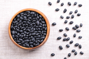 Black beans in a wooden bowl on linen. Dried variety of common beans, Phaseolus vulgaris, also known as black turtle beans, and caviar criollo. Type of bean with satiny black skin and a white center.