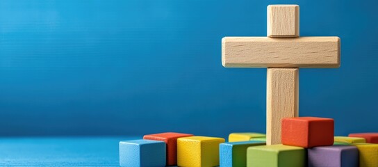 Wooden cross and colorful building blocks on a blue background, with copy space for a Christian social media banner design concept.