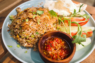 Tasty and famous Indonesian traditional fried rice with sambal and fresh vegetables served on table at an outdoor restaurant for lunch, looking delicious and tempting