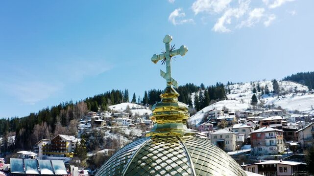 Drone footage of a shiny cross in a small mountain town in the winter
