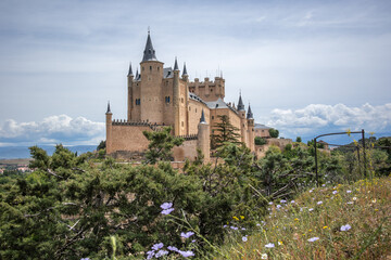 Alcazar of Segovia from Beautiful Viewpoint with Flowers in Spain. Architectural Exterior of Medieval Castle in Europe.