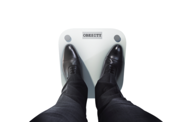 Businessman's feet in black shoes on a weight scale labeled obesity, closeup style on white background, concept of health and weight issues